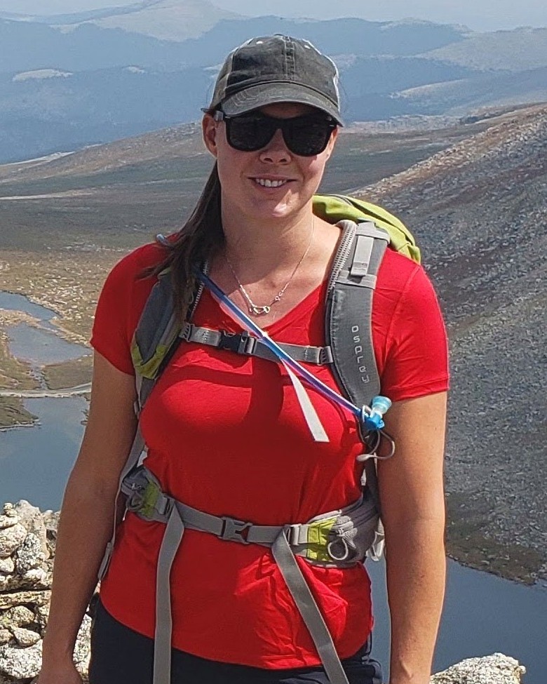 Jessica Isbrecht, Sales at Kudurru Stone, on a mountain summit above an alpine lake.